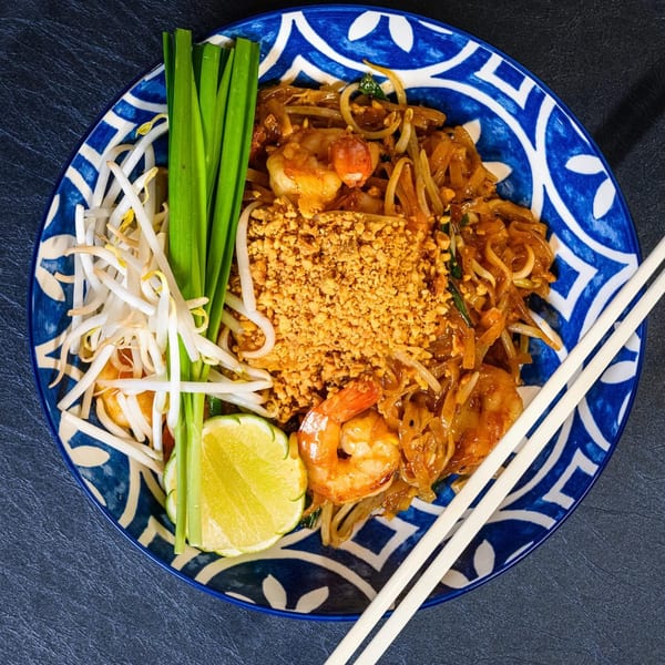 Chili Basil Thai Cuisine's Pad Thai with shrimp, peanuts, bean sprouts, chives, and lime on a blue plate.