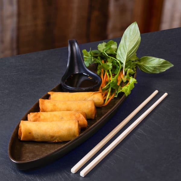 Crispy Thai spring rolls with dipping sauce, fresh herbs, and chopsticks on a dark plate.