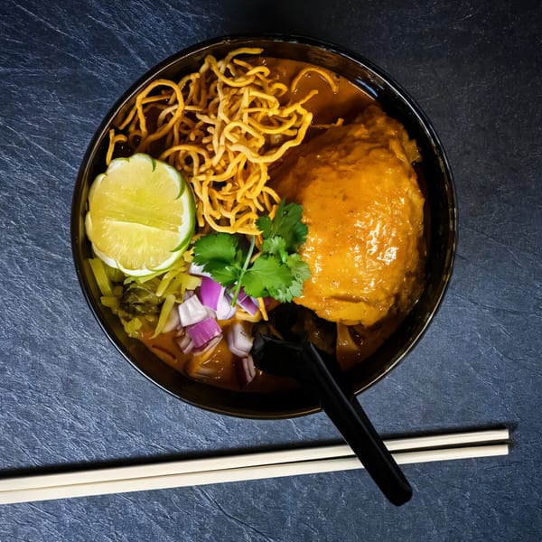 A bowl of Khao Soi, a Thai curry noodle soup, with chicken, crispy noodles, and lime.