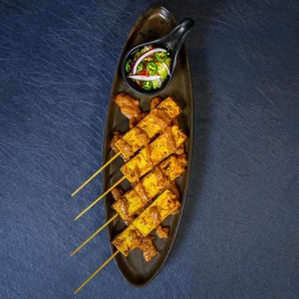 Thai tofu satay skewers with peanut sauce and a side of pickled vegetables on a dark plate.