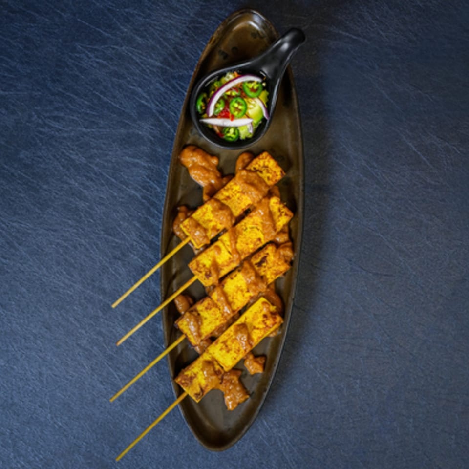 Thai tofu satay skewers with peanut sauce and a side of pickled vegetables on a dark plate.